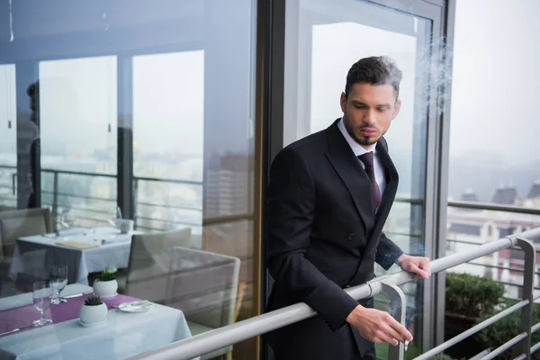 Portrait of young man in suit smoking at restaurant balcony — Stock Photo