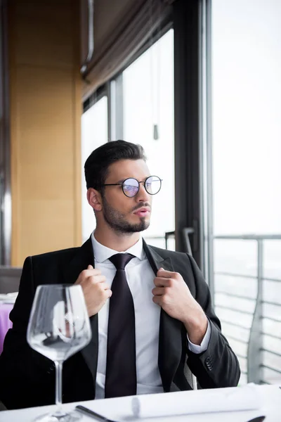 Задумчивый человек в костюме и очках смотрит в сторону в ожидании порядка в ресторане — стоковое фото