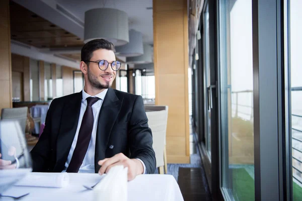 Uomo sorridente in giacca e cravatta e occhiali distogliendo lo sguardo in attesa di ordine nel ristorante — Foto stock