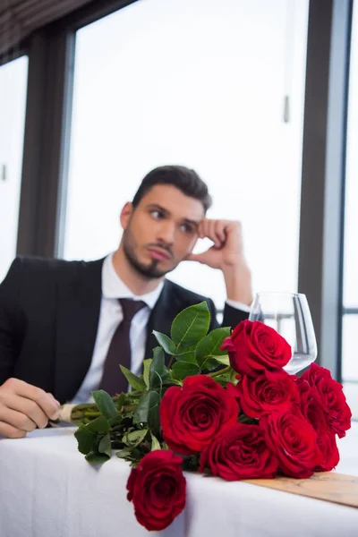 Selective focus of man in suit with bouquet of red roses waiting for girlfriend in restaurant — Stock Photo