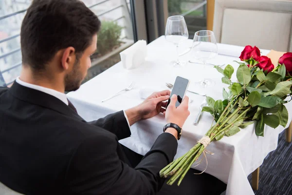 Side view of man in suit using smartphone while waiting for girlfriend in restaurant — Stock Photo