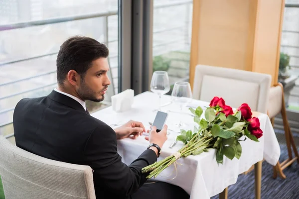 Молодой человек в костюме со смартфоном ждет подругу в ресторане — стоковое фото