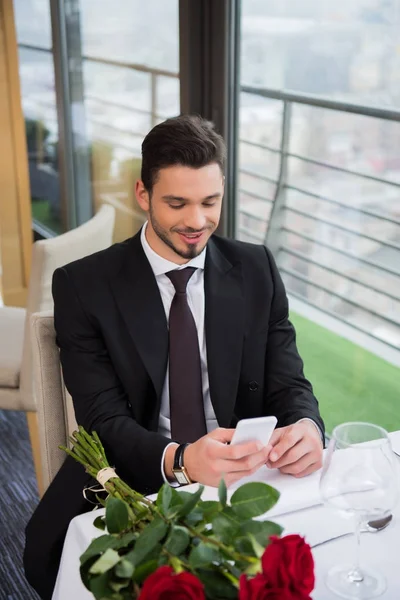 Portrait of smiling man in suit using smartphone while waiting for girlfriend in restaurant — Stock Photo
