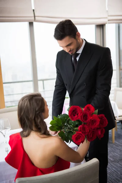 Частковий вид чоловіка, що представляє букет з троянд дівчині в ресторані на день святого Валентина — стокове фото