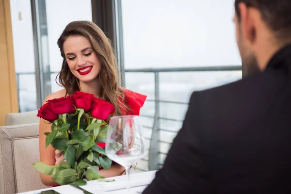 Mujer sonriente con ramo de rosas durante la cita romántica con el novio en el restaurante, día de San Valentín - foto de stock