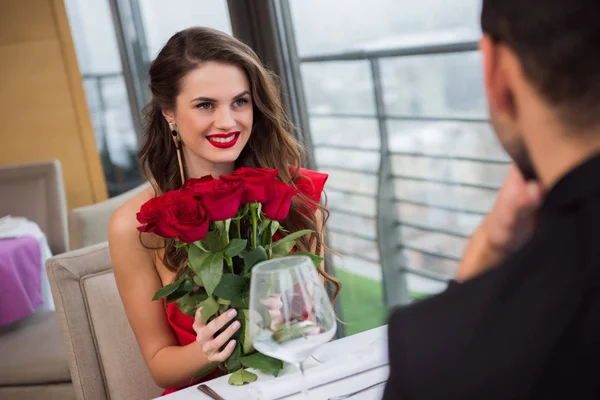 Mulher sorridente com buquê de rosas durante encontro romântico com namorado no restaurante, dia de São Valentim — Fotografia de Stock