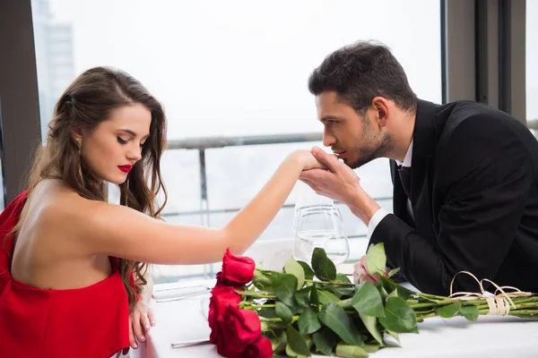Vista lateral del hombre besar novias mano durante la fecha en San Valentín día en el restaurante - foto de stock