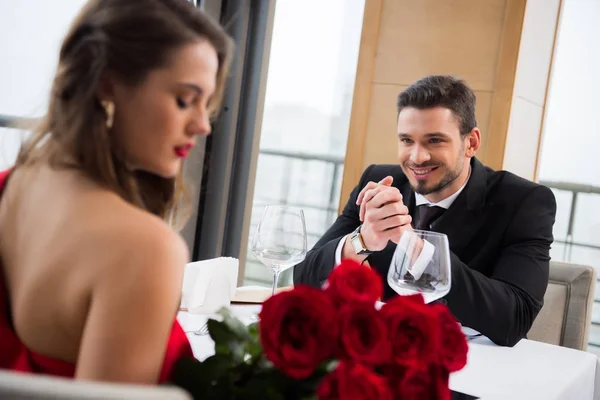 Foyer sélectif de sourire homme regardant petite amie avec bouquet de fleurs dans le restaurant, st Saint-Valentin — Photo de stock