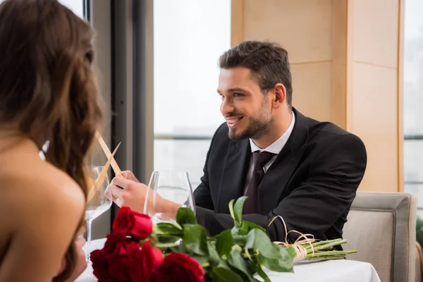 Vista parcial del hombre sonriente mirando a la novia mientras lee el menú en la cita romántica en el restaurante, día de San Valentín - foto de stock