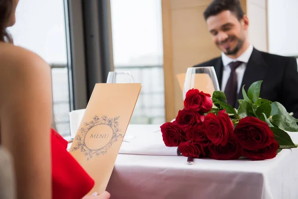 Foco selectivo del menú de lectura de pareja en la cita romántica en el restaurante en el día de San Valentín - foto de stock