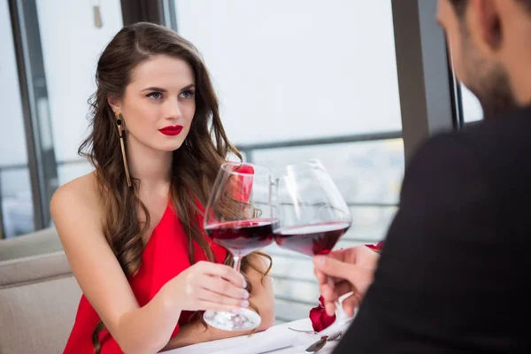 Partial view of couple clinking glasses of red wine during romantic date in restaurant — Stock Photo