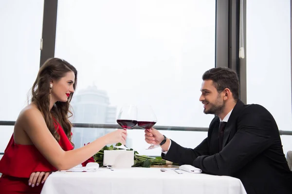 Боковой вид на пару звон бокалов красного вина во время празднования Дня Святого Валентина в ресторане — стоковое фото