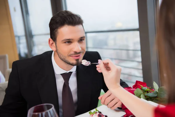 Partial view of woman feeding boyfriend with dessert on st valentine day romantic date in restaurant — Stock Photo