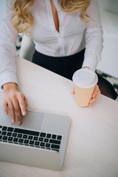 Imagen recortada de la mujer de negocios sosteniendo taza de café desechable y el uso de ordenador portátil - foto de stock