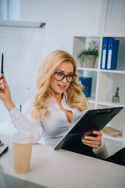 Atractiva mujer de negocios leyendo documentos en el portapapeles - foto de stock