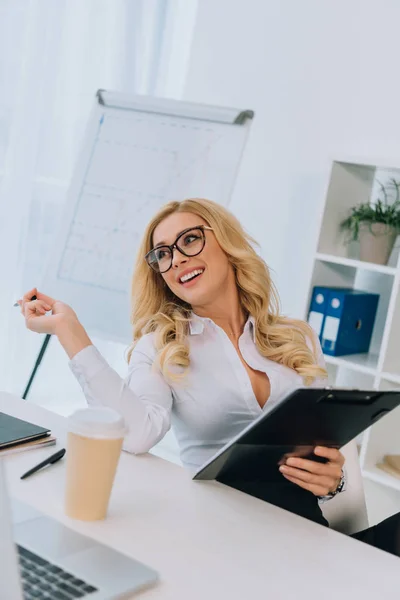 Sonriente sexy mujer de negocios sosteniendo documentos en el portapapeles - foto de stock