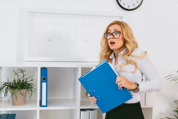 Femme choquée debout avec dossier au bureau — Photo de stock