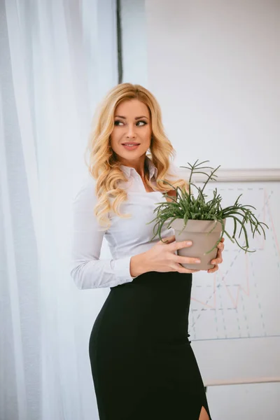 Femme d'affaires tenant le pot de fleurs avec la plante verte et regardant loin — Photo de stock