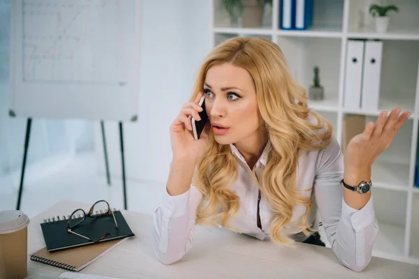 Irritated businesswoman talking by smartphone in office — Stock Photo