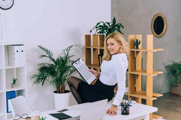 Verführerische Frau, die mit Dokumenten am Tisch sitzt und in die Kamera blickt — Stockfoto