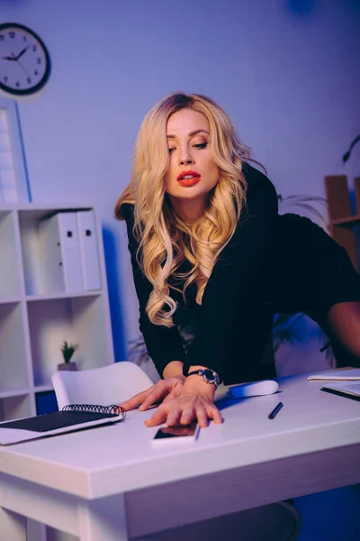 Sexy blonde woman reaching for smartphone on table — Stock Photo