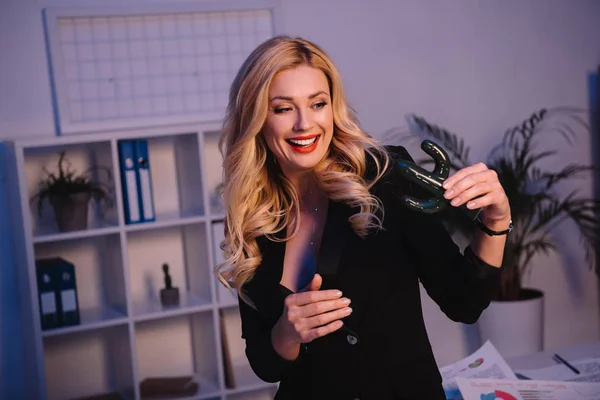 Sonriente sexy mujer de negocios sosteniendo cactus artificiales en la oficina - foto de stock