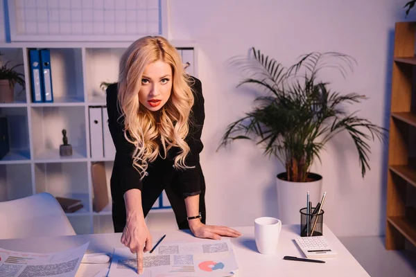 Femme d'affaires en colère pointant sur les documents sur la table et regardant la caméra — Photo de stock