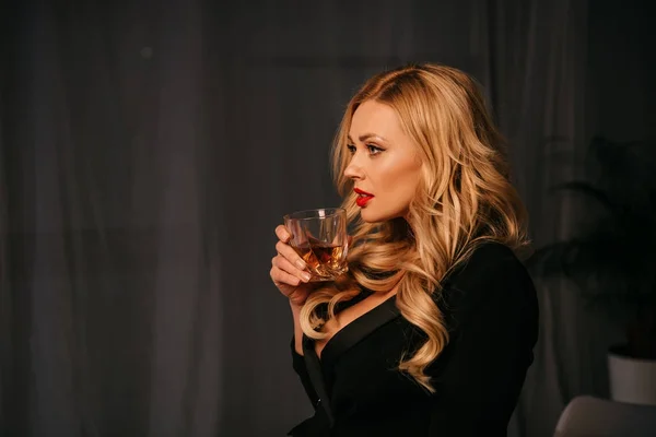 Side view of attractive sexy blonde woman drinking whiskey in office at evening — Stock Photo