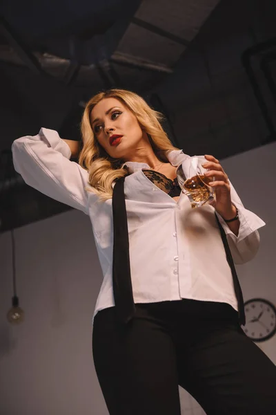 Bottom view of seductive woman posing and standing with glass of whiskey — Stock Photo