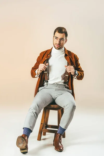 Handsome pensive man looking away while sitting on wooden chair, on beige — Stock Photo