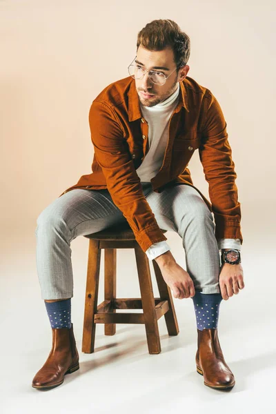Красивий чоловік сидить на дерев'яному стільці і зав'язує шкарпетки, на бежевому — стокове фото