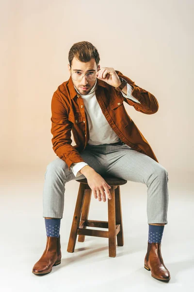 Schöner Mann sitzt auf einem Holzstuhl und schaut in die Kamera, auf beige — Stockfoto