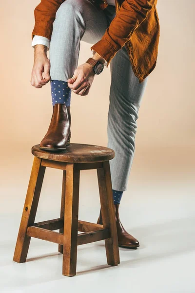 Частковий вид людини, що зв'язує шнурки, стоячи на дерев'яному стільці з однією ногою — стокове фото