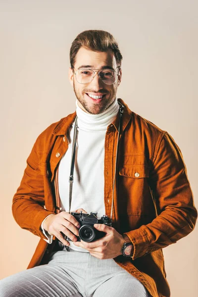 Portrait of cheerful man in stylish clothing with photo camera looking at camera isolated on beige — Stock Photo