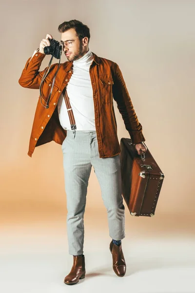 Homem elegante com mala tirando foto na câmera fotográfica — Fotografia de Stock
