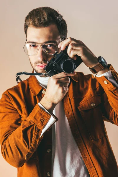 Портрет модного молодого чоловіка в окулярах з фотоапаратом, ізольований на бежевому — стокове фото