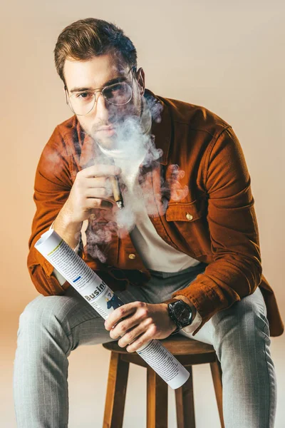 Retrato de hombre de negocios con estilo con cigarro y periódico de negocios en manos aisladas en beige - foto de stock