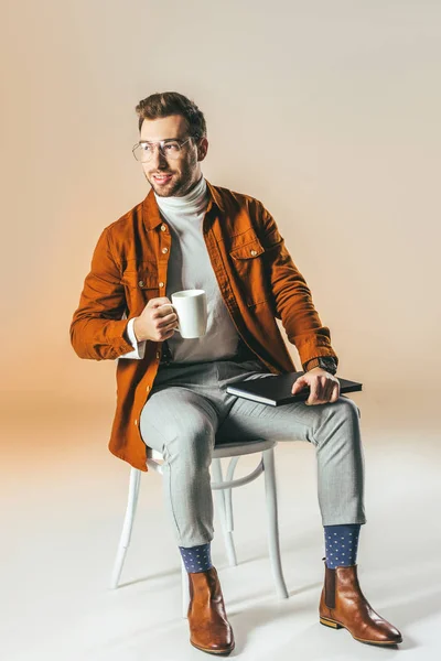 Uomo sorridente con tazza di caffè e taccuino seduto sulla sedia — Foto stock