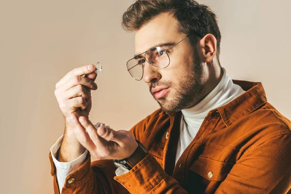 Side view of fashionable man looking at diamond in hand isolated on beige — Stock Photo