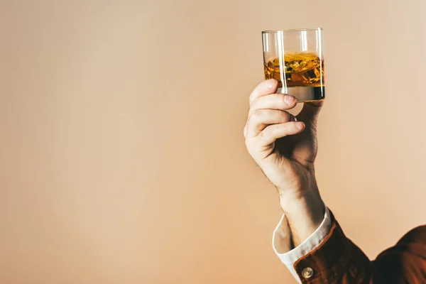 Cropped shot of man holding glass of whiskey isolated on beige — Stock Photo