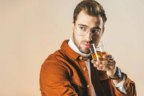 Retrato de homem na moda pensativo com vidro de uísque desviando o olhar isolado em bege — Fotografia de Stock