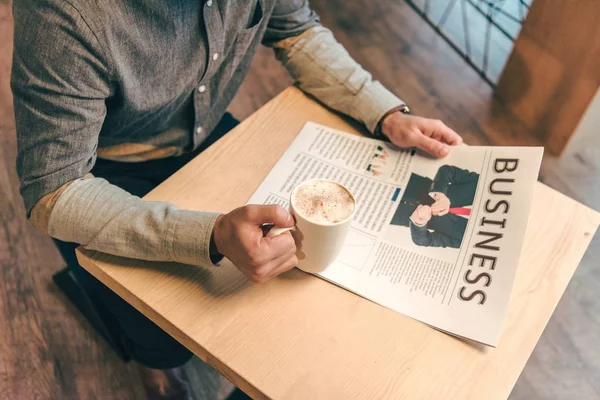 Vista parcial del empresario con taza de café y periódico de negocios en la cafetería - foto de stock