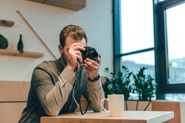 Vista oscura del hombre tomando fotos en la cámara fotográfica en la cafetería - foto de stock