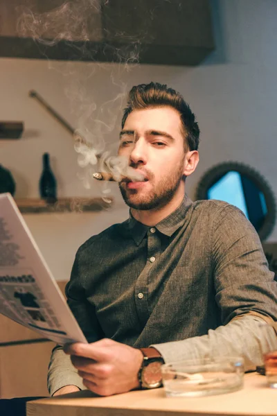 Portrait of confident businessman with newspaper smoking cigar in cafe — Stock Photo