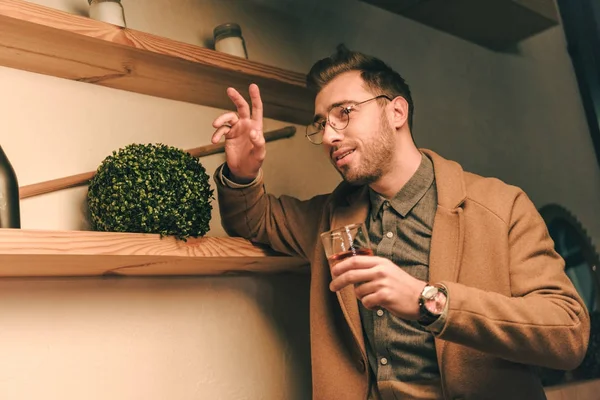 Seitenansicht eines modischen Mannes mit einem Glas Whiskey, der jemandem im Café zuwinkt — Stockfoto