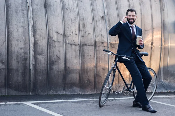 Empresário alegre com café para ir falar no smartphone na rua — Fotografia de Stock