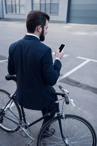 Back view of businessman using smartphone while leaning on bicycle on street — Stock Photo