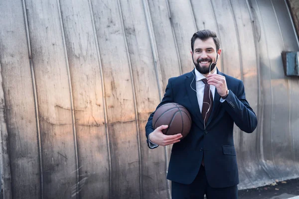 Ritratto di un uomo d'affari sorridente in auricolare con pallone da basket in strada — Foto stock
