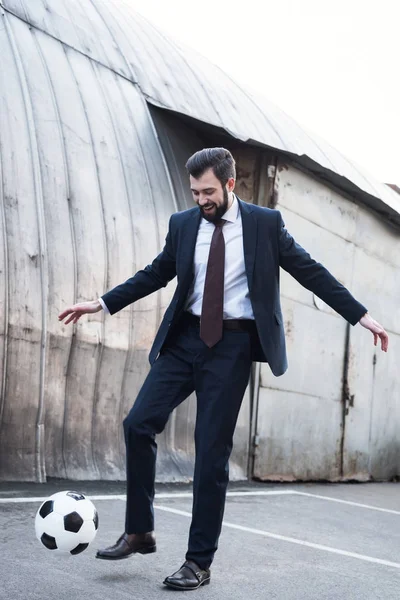 Homme d'affaires souriant en costume jouant au football dans la rue — Photo de stock