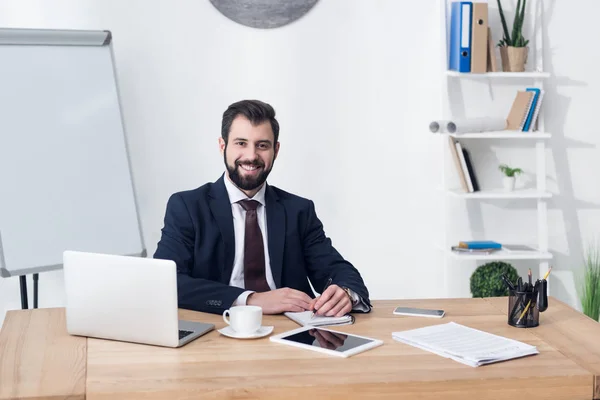 Portrait of smiling businessman looking at camera while sitting at workplace in office — Stock Photo